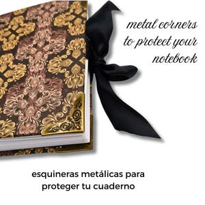 Puede incluir: Un cuaderno decorativo con un estampado floral marr&oacute;n y dorado, esquinas met&aacute;licas doradas y una cinta de raso negra. El texto dice "metal corners to protect your notebook".