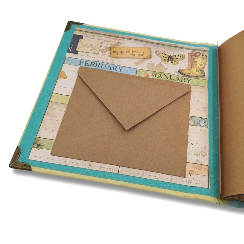 May include: Open scrapbook with a brown envelope, a butterfly, and a yellow boot illustration. The scrapbook has a blue border and metal corner protectors. The text "my garden feeds my soul" is visible.