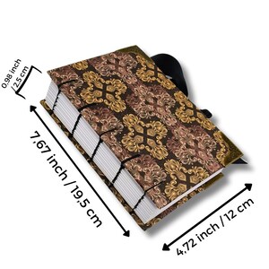 Puede incluir: Un diario hecho a mano con una cubierta decorativa con un estampado floral marr&oacute;n y dorado. El diario mide 19,5 cm de largo, 12 cm de ancho y 2,5 cm de grosor. Tiene un cierre de cinta negra y encuadernaci&oacute;n cosida.