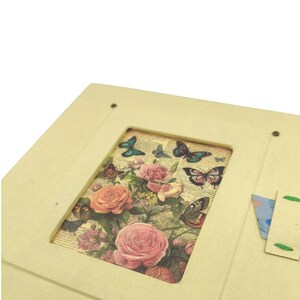 May include: A cream-colored, rectangular box with a rectangular cutout revealing a floral and butterfly design. The design features pink roses and various butterflies in shades of blue, brown, and green. The box has a small, attached flap.