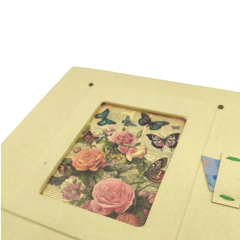 May include: A cream-colored, rectangular box with a rectangular cutout revealing a floral and butterfly design. The design features pink roses and various butterflies in shades of blue, brown, and green. The box has a small, attached flap.