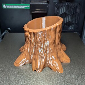 May include: A brown, tree stump-shaped planter. The planter has a textured, bark-like exterior and a smooth interior. The planter is sitting on a gray surface.