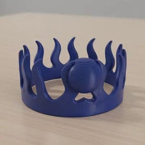 May include: A 3D-printed, royal blue crown with a unique design. The crown features stylized flame-like points around the perimeter and a central, spherical element. The object is likely a decorative piece or a costume accessory.
