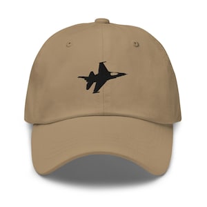 Peut inclure: Une casquette de baseball beige avec une silhouette de jet de combat brodée en noir.