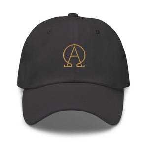 May include: A dark gray baseball cap with a gold embroidered design featuring the letters "A" and "Ω". The cap has a curved brim and a fabric strap closure on the back. This hat is a stylish accessory.