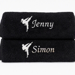 May include: Two black towels stacked vertically, each featuring white embroidery of a person performing a martial arts kick. The top towel is personalised with the name Jenny, and the bottom towel is personalised with the name Simon in white text.