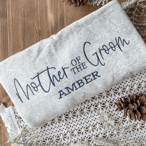 May include: Gray sweatshirt with the text "Mother of the Groom Amber" embroidered in navy blue.