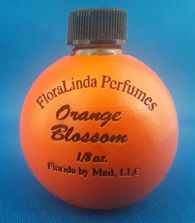 Puede incluir: Una peque&ntilde;a botella de vidrio naranja con una tapa negra. La botella est&aacute; etiquetada con "FloraLinda Perfumes Orange Blossom 1/8 oz. Florida by Mail, LLC".