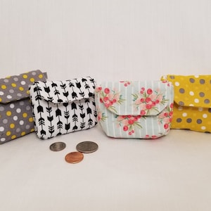 May include: Four small, square fabric coin purses with flap closures. Patterns include gray with yellow polka dots, black arrows on white, floral on blue stripes, and yellow with gray polka dots. Coins are visible in front.