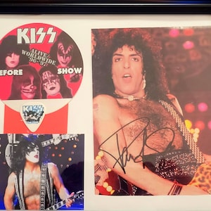 Op de afbeelding: Een ingelijste foto van KISS-bandlid Paul Stanley, met een gesigneerde handtekening. De foto is van de "Alive/Worldwide"-tour van de band uit 1996-1997. De lijst bevat ook een KISS-logo sticker en een plectrum.