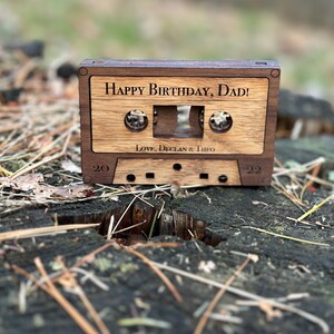 May include: A wooden cassette tape with the text "Happy Birthday, Dad! Love, Declan & Theo" on the front. The cassette tape is sitting on a tree stump.