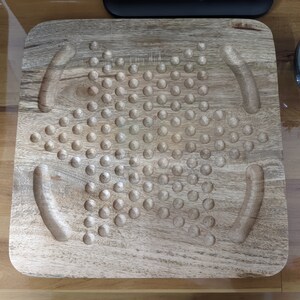 May include: A wooden game board with a star-shaped pattern of holes. The board has two curved indentations on either side of the star.