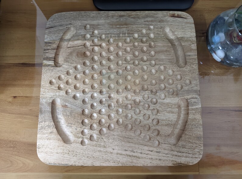 May include: A wooden game board with a star-shaped pattern of holes. The board has two curved indentations on either side of the star.