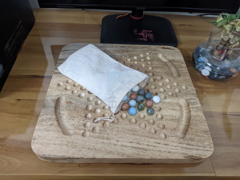 May include: A wooden game board with a white cloth bag filled with colorful marbles. The board has a large number of holes and two curved grooves.