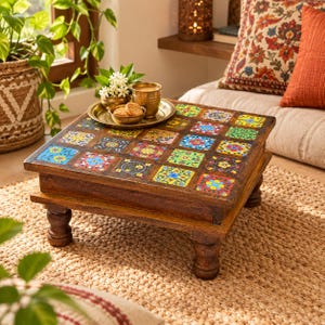 Puede incluir: Una mesa baja cuadrada de madera con una superficie superior incrustada con dieciséis azulejos pintados a mano con coloridos motivos florales. La mesa se apoya sobre cuatro patas cortas y redondeadas, hecha de madera marrón oscura.