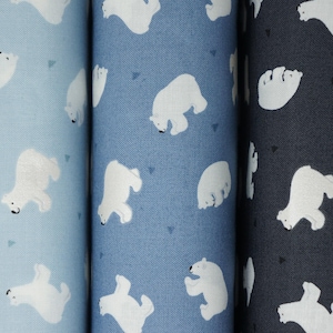 May include: Three rolls of fabric featuring a repeating pattern of white polar bears and small dark triangles. The fabric rolls are arranged side-by-side in a gradient of colors, transitioning from light blue to medium blue to a dark navy blue.