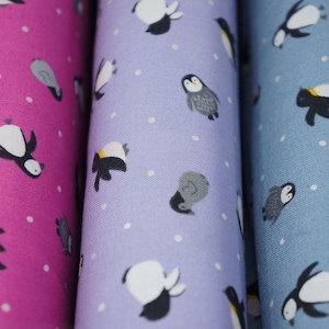 May include: Three rolls of fabric featuring a repeating pattern of small penguins and white dots. The left roll is magenta, the center roll is light purple, and the right roll is light blue. Each penguin is depicted in black, white, and gray.