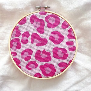 May include: A pink and white leopard print embroidery hoop with a wooden frame.