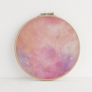 May include: A pink and purple galaxy-themed embroidery hoop with a white background. The hoop is made of wood and has a gold metal ring.