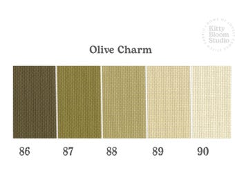 Op de afbeelding: Een kleurenpalet getiteld Olive Charm met vijf verticale stofstalen met een geweven textuur. De kleuren variëren van donker olijfgroen tot licht crème, gelabeld met de nummers 86, 87, 88, 89 en 90. Het logo van Kitty Bloom Studio is zichtbaar.