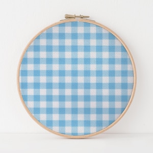 May include: A round embroidery hoop featuring a blue and white gingham pattern. The fabric is stretched taut within a natural wood hoop, creating a classic, handcrafted look. The design evokes a sense of traditional craft and home decor.
