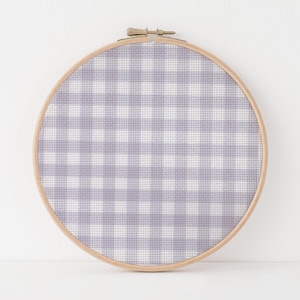 May include: A round embroidery hoop with a light purple and white gingham pattern. The fabric is stretched taut within a natural wood hoop, secured with a metal clasp. The design features a classic checkered pattern, perfect for home decor.
