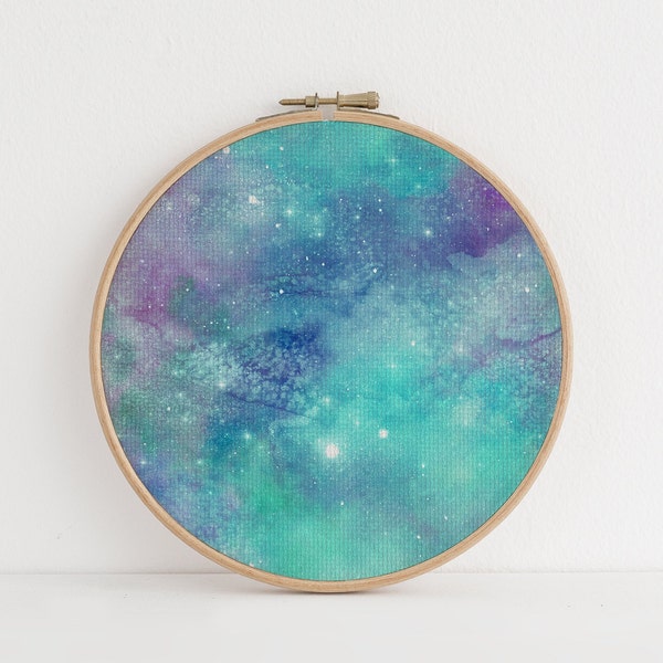 May include: A round wooden embroidery hoop with a watercolor painting of a galaxy. The galaxy is a mix of blue, green, and purple colors with white stars.