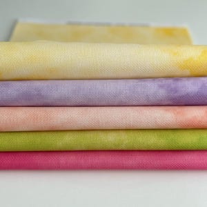 May include: Five pieces of fabric in various shades of yellow, purple, pink, green, and red. The fabric is folded and stacked on top of each other.