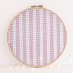 May include: A circular embroidery hoop featuring a pink and white striped design. The fabric is stretched within a wooden hoop. The pattern consists of vertical stripes, offering a simple, yet attractive look. This is a craft item, suitable for embroidery projects.