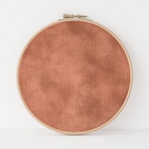 May include: A round wooden embroidery hoop with a terracotta-colored fabric stretched across the frame.