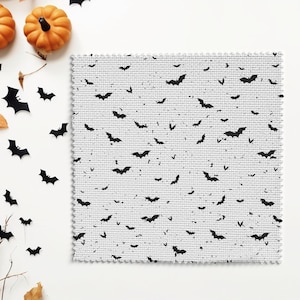 May include: A white fabric with a black bat pattern. The fabric is textured and has a subtle sheen. The bats are scattered randomly across the fabric.