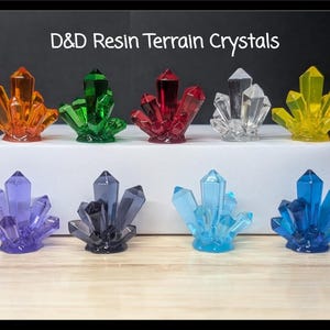 May include: A collection of resin terrain crystals in various colors, including orange, green, red, clear, yellow, purple, gray, light blue, and dark blue. The crystals are arranged on a white surface, with the text "D&D Resin Terrain Crystals" at the top.