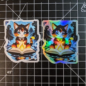 May include: A holographic sticker featuring a cartoon cat with orange and black fur sitting on an open book. The cat is surrounded by flames and water. The sticker is on a black and white grid background.