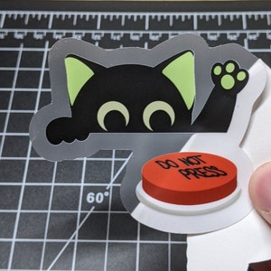 May include: A black cat with green ears peeks over a red button that says "Do Not Press".