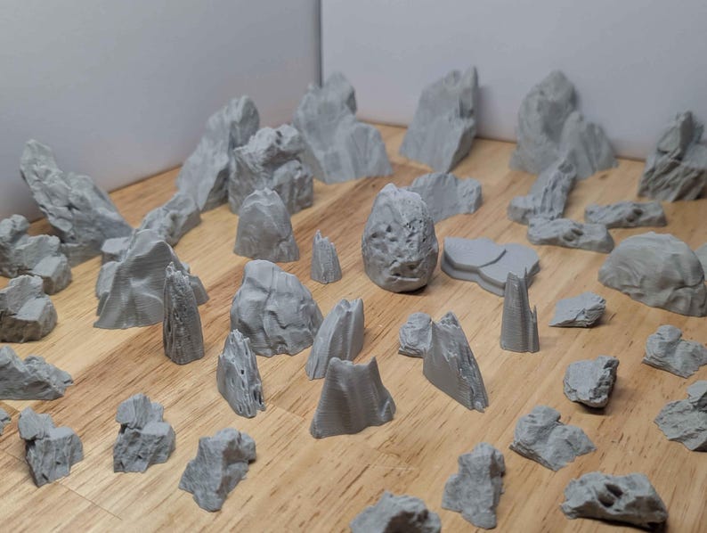 May include: A selection of grey miniature rock formations in various sizes and shapes. The rocks are arranged on a wooden surface, with some upright and others flat. The rocks have a textured appearance.