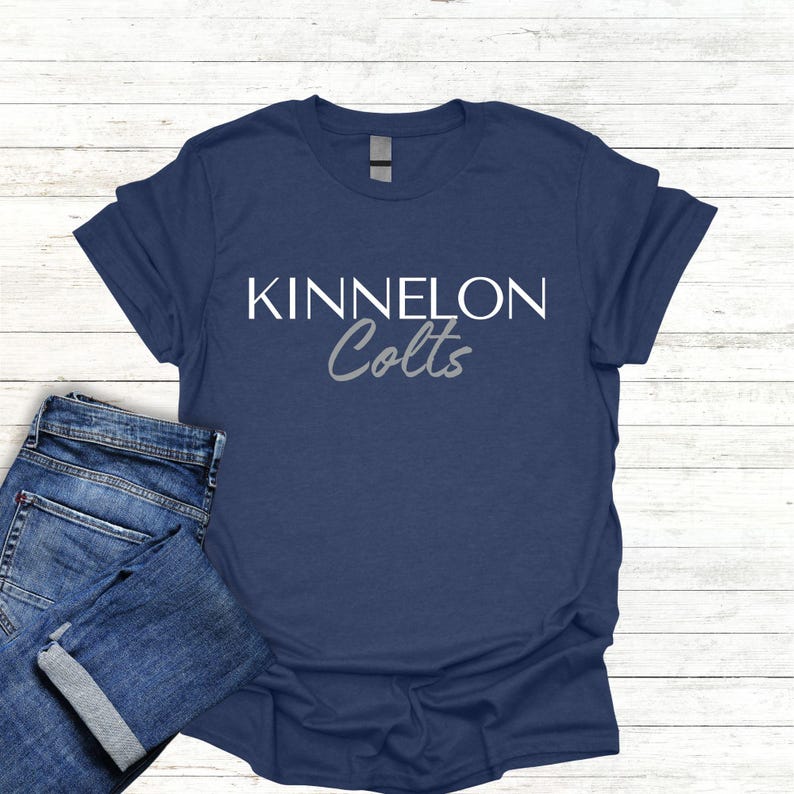 K&ouml;nnte beinhalten: Ein marineblaues T-Shirt mit wei&szlig;em Text, der "KINNELON Colts" in einer wei&szlig;en serifenlosen Schriftart lautet. Das Wort "Colts" ist in einer grauen Kursivschrift.
