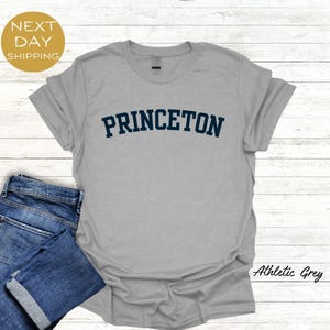 May include: A gray t-shirt with the word "PRINCETON" printed in blue on the front. The shirt is made of a soft, comfortable material and is perfect for everyday wear.