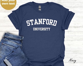 Pode incluir: Uma t-shirt azul-marinho de manga curta com o texto branco STANFORD UNIVERSITY numa fonte universitária, combinada com um par de calças de ganga azuis. Um gráfico circular dourado no canto superior esquerdo contém o texto Add your own text.