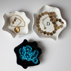 May include: Three ceramic dishes in the shape of a star with scalloped edges. The dishes are white with a gold necklace with a pendant in one, a gold necklace with round links in another, and a turquoise necklace in the third.