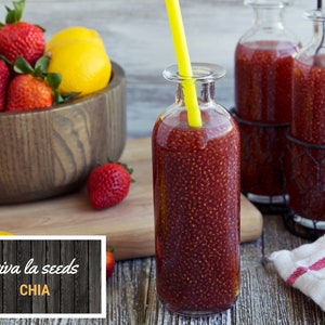 May include: A glass bottle filled with red chia seed pudding with a yellow straw sticking out of the top. The bottle is sitting on a wooden table next to a bowl of strawberries and a lemon. The text "viva la seeds CHIA" is on a wooden sign in the lower left corner of the image.