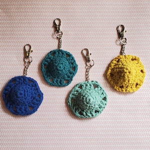 May include: Four crocheted keychains in different colors: blue, teal, light green, and yellow. Each keychain has a silver metal ring and chain.