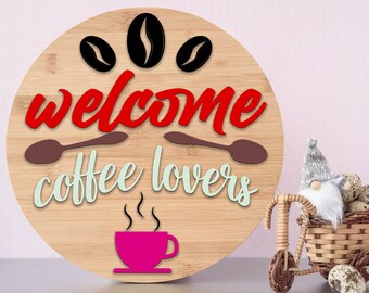 Könnte beinhalten: Rundes Holzschild mit dem Text "welcome coffee lovers" in roten und grünen Buchstaben. Oben auf dem Schild sind drei schwarze Kaffeebohnen. Unten auf dem Schild befindet sich eine rosa Kaffeetasse mit Dampf.