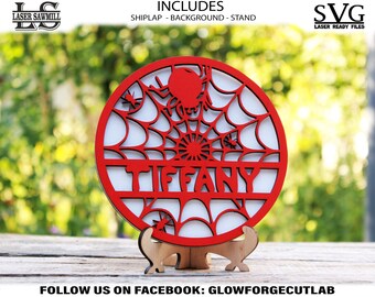 Puede incluir: Círculo de madera rojo con un diseño de telaraña y el nombre "TIFFANY" recortado. El círculo está sobre un soporte de madera.