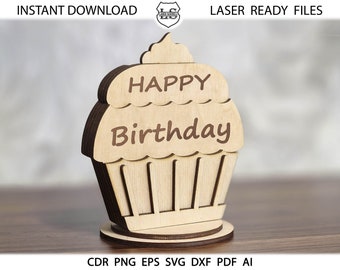 May include: A wooden cupcake cutout with the words "Happy Birthday" on it. The cupcake is brown and has a white frosting top. The cutout is on a wooden base.