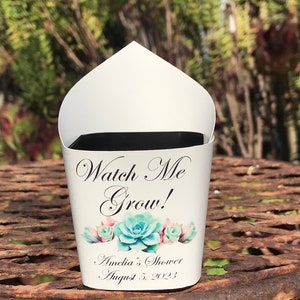 May include: White paper cone with a black rim, decorated with a green and pink succulent design. The text "Watch Me Grow!" is printed in black cursive font. Below the succulents, the text "Amelia's Shower August 5, 2023" is printed in black.