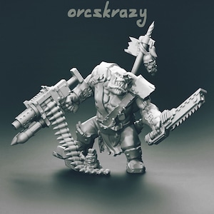 Puede incluir: Una figura miniatura gris sin pintar de un guerrero orco con el texto orcskrazy encima. La figura sostiene un arma de fuego grande con una larga cinta de munición que llega al suelo y una espada sierra en la otra mano, con un estandarte en la espalda.