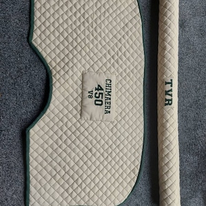 May include: Beige quilted car cover with green trim and a cylindrical roll. The cover has a patch with the text "CHIMARA 450 V8". The roll has the text "TYR".