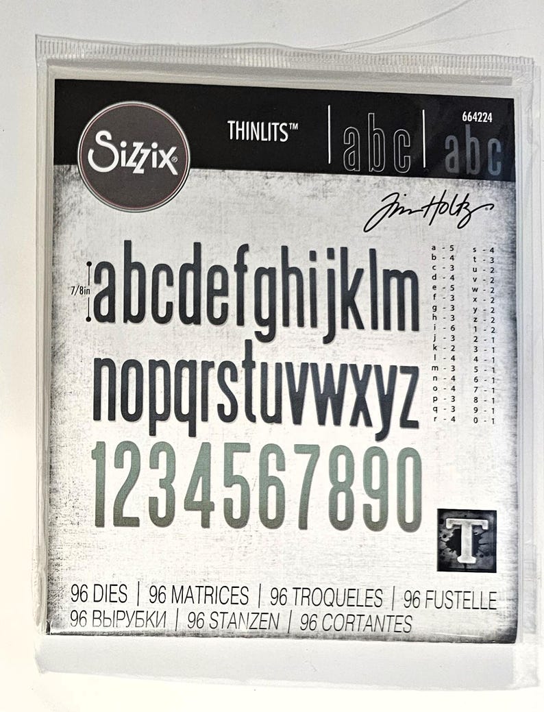 Op de afbeelding: Een pakket Sizzix Thinlits stansmessen met het alfabet en cijfers. De letters en cijfers zijn in een schreefloze lettertype, ongeveer 2.2 cm hoog. Het pakket bevat 96 stansmessen en de tekst "Jim Holtz".