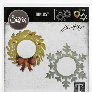 Peut inclure: Un ensemble de deux pochoirs en métal découpés pour l'artisanat. Les pochoirs présentent une couronne avec des baies rouges et un motif de flocon de neige. L'emballage comprend le texte "THINLITS TM" et "Jim Holtz".