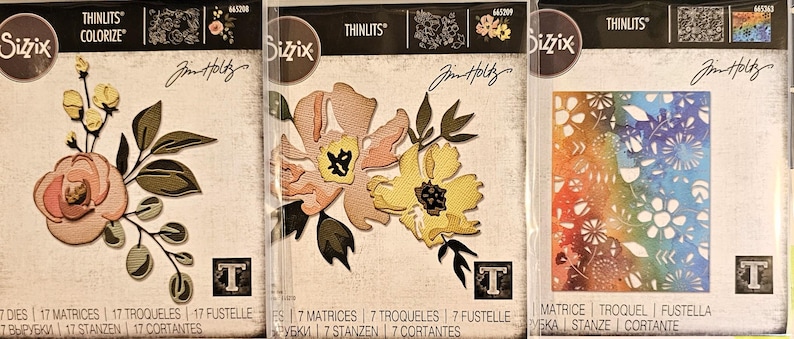 May include: Three Sizzix Thinlits die sets featuring floral designs. The sets include die-cut flowers and leaves in various colors, including pink, yellow, and green. The packaging includes the text "COLORIZE" and "Jim Holtz".